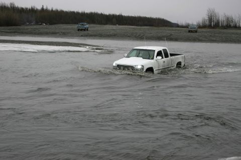 2003 Jeep TJ - White GMC Sierra pickup truck navigates through water with another vehicle visible in the distance.