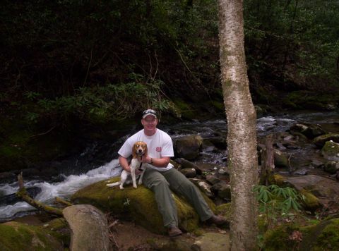 1995 Ford Bronco - A man and his beagle enjoy a moment by a flowing stream in a wooded area.