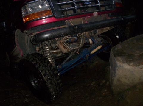 1995 Ford Bronco - This red Ford Bronco's front suspension and tire are visible, positioned near a large rock.