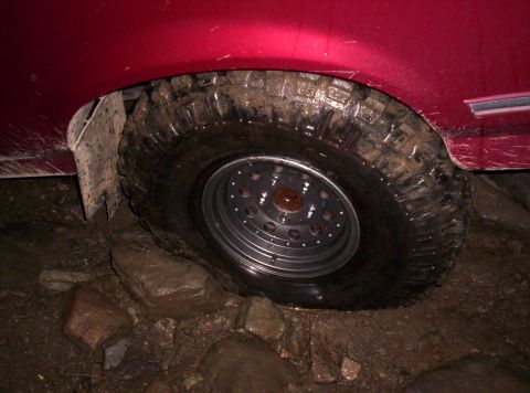 1995 Ford Bronco - A close-up of a red SUV's tire and wheel navigating rocky terrain.
