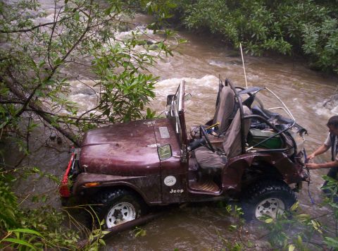 1995 Ford Bronco - A Jeep is stuck in a fast-moving river, with branches and debris around it.