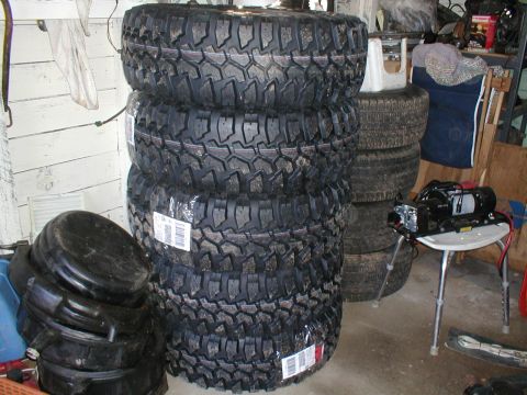 1979 Ford Bronco - A stack of four new off-road tires sits next to other used tires and a winch.