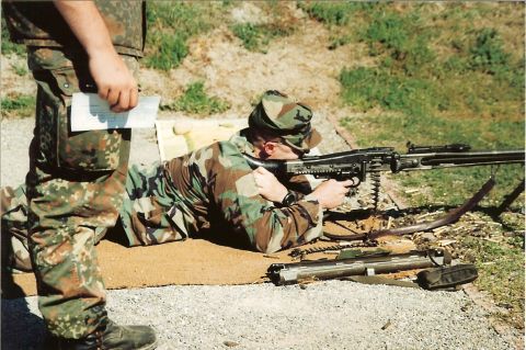 2003 Jeep TJ - Two soldiers in camouflage uniforms are at a firing range, one aiming a machine gun while the other holds a document.