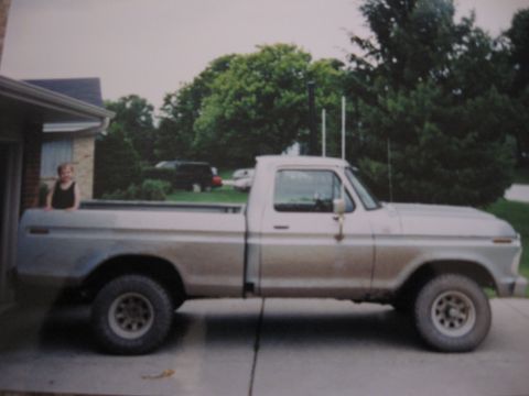 1977 Ford F-150 - A child stands in the bed of a silver pickup truck parked in front of a house.