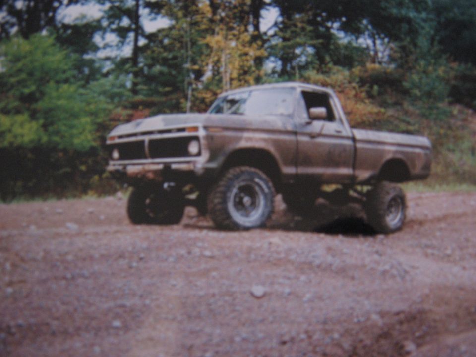 Lifted brown pickup truck on a dirt road with trees in the background