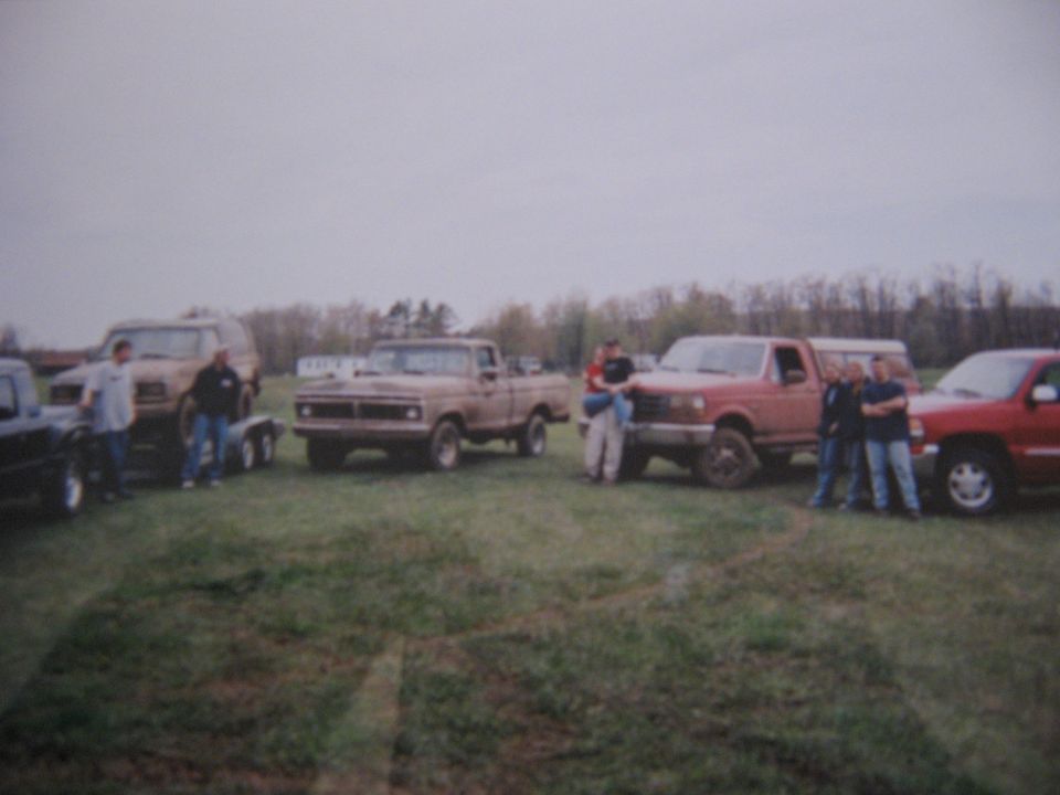 Several pickup trucks and an SUV parked in a grassy field with people standing around them