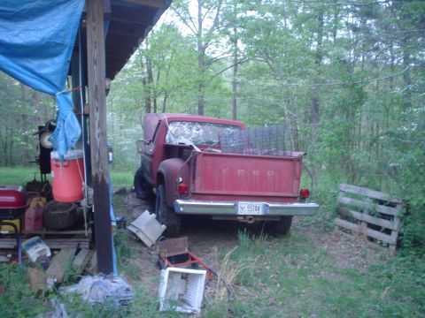 1976 Ford F-100 - A red Ford pickup truck is parked outdoors, partially covered by a blue tarp.