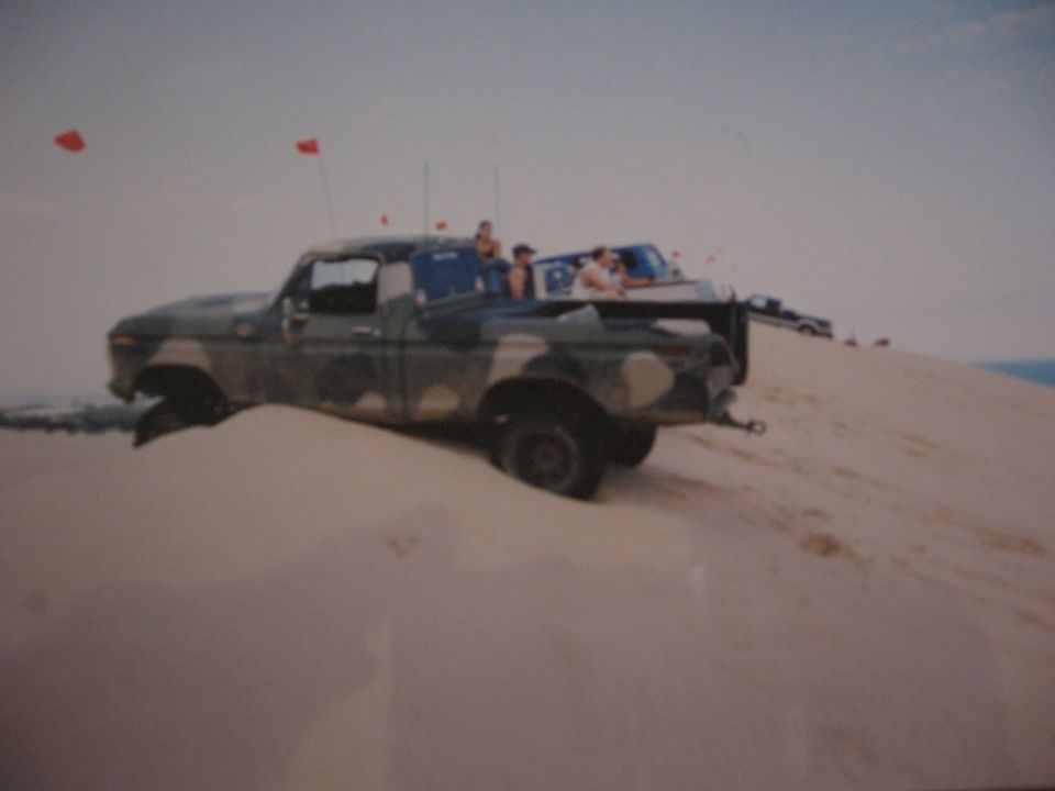 1977 Ford F-150 pickup truck with camouflage paint on a sand dune, with another truck behind it