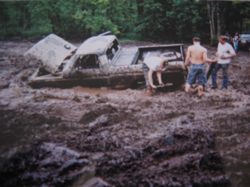 Mud-covered 1977 Ford F-150 stuck in deep mud with hood open