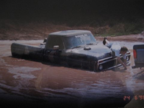 1977 Ford F-150 - A 1977 Ford F-150 is partially submerged in mud with a person attempting to free it.