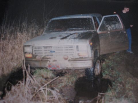 1977 Ford F-150 - A truck is stuck in a muddy ditch, with a person standing by the open door.