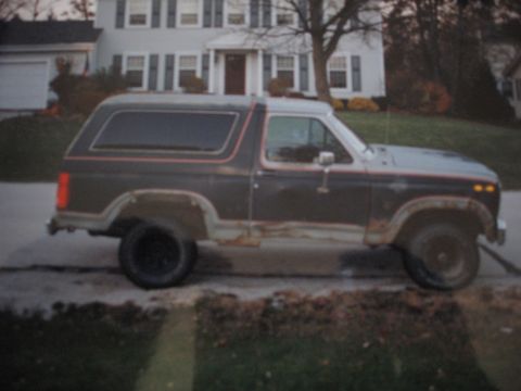 1977 Ford F-150 - Side view of a dark brown Ford Bronco with red trim, exhibiting rust on its lower body panels.