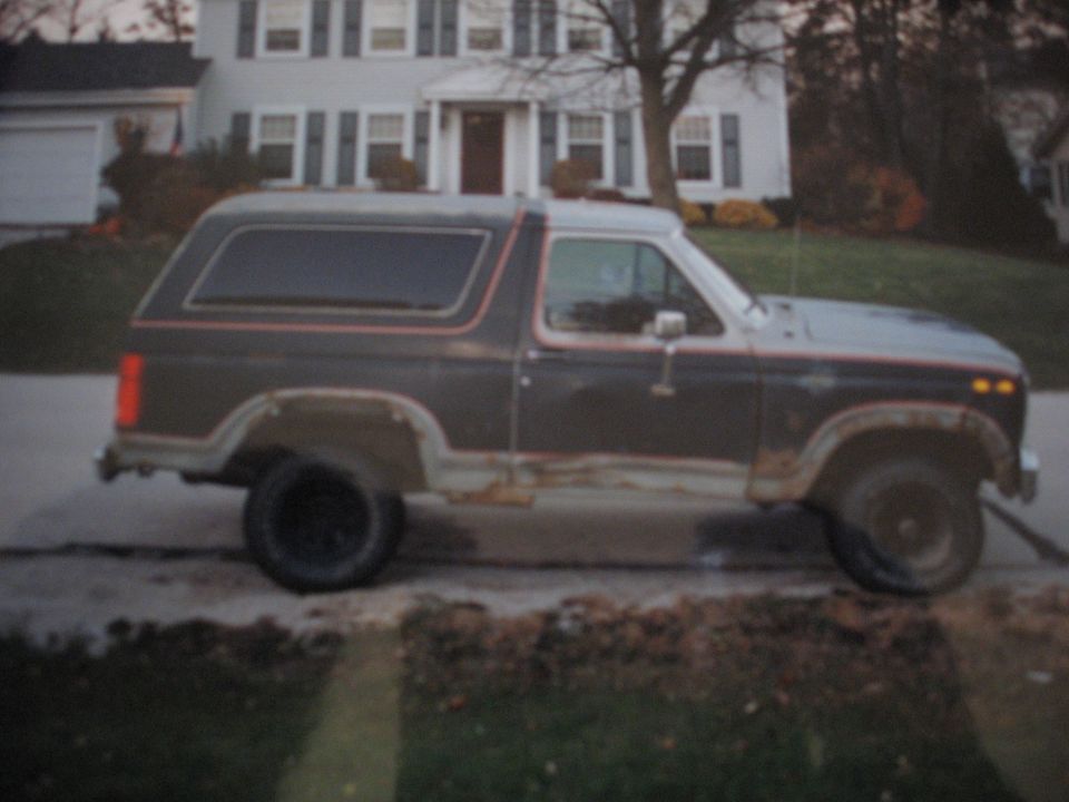 Dark brown Ford Bronco with red trim, showing rust on lower body panels, parked on a driveway