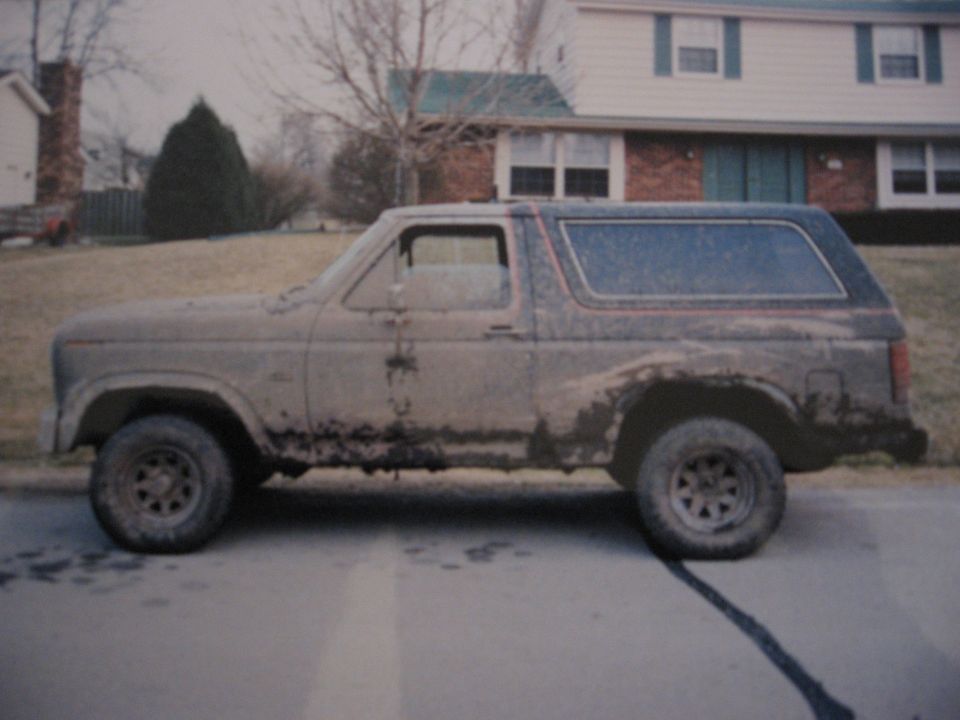 Side view of a dirty, second-generation Ford Bronco parked on a street