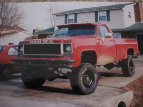 1977 Ford F-150 - This red pickup truck has a lifted suspension and large off-road tires, with a visible "DAMAGE INC." decal on the front.