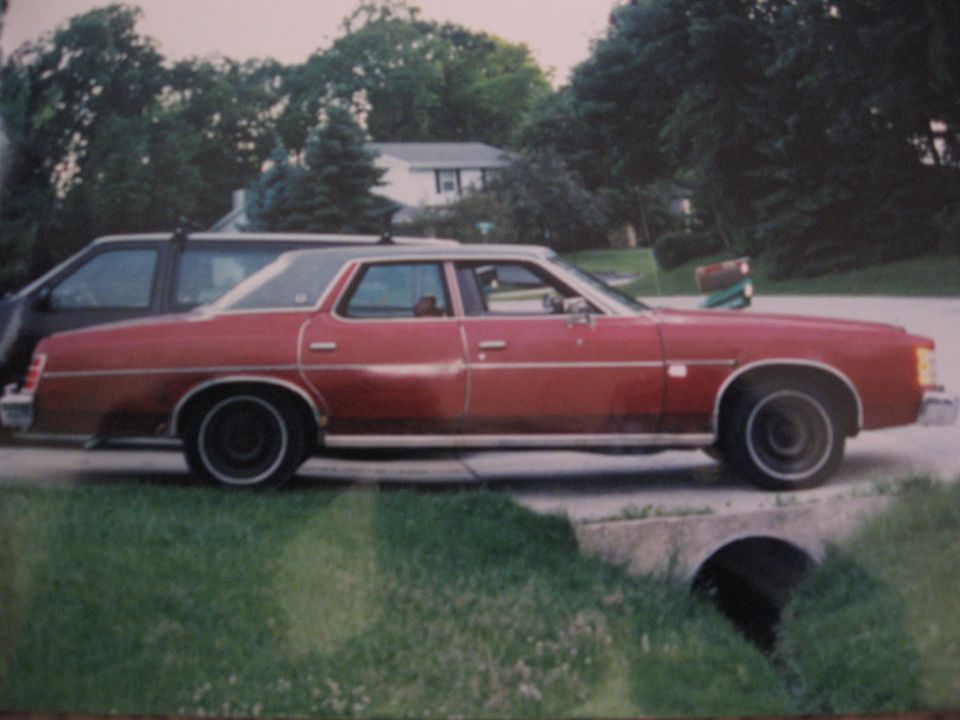 Red sedan with a vinyl roof parked next to a dark SUV