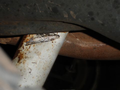 1989 Ford Bronco - Undercarriage view shows a rusty exhaust pipe and a painted bracket with signs of wear and tear.
