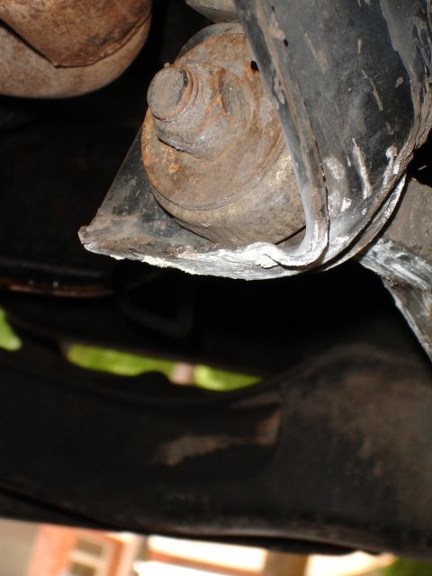 1989 Ford Bronco - A heavily corroded suspension component is visible from underneath a vehicle, with some white residue on the metal.