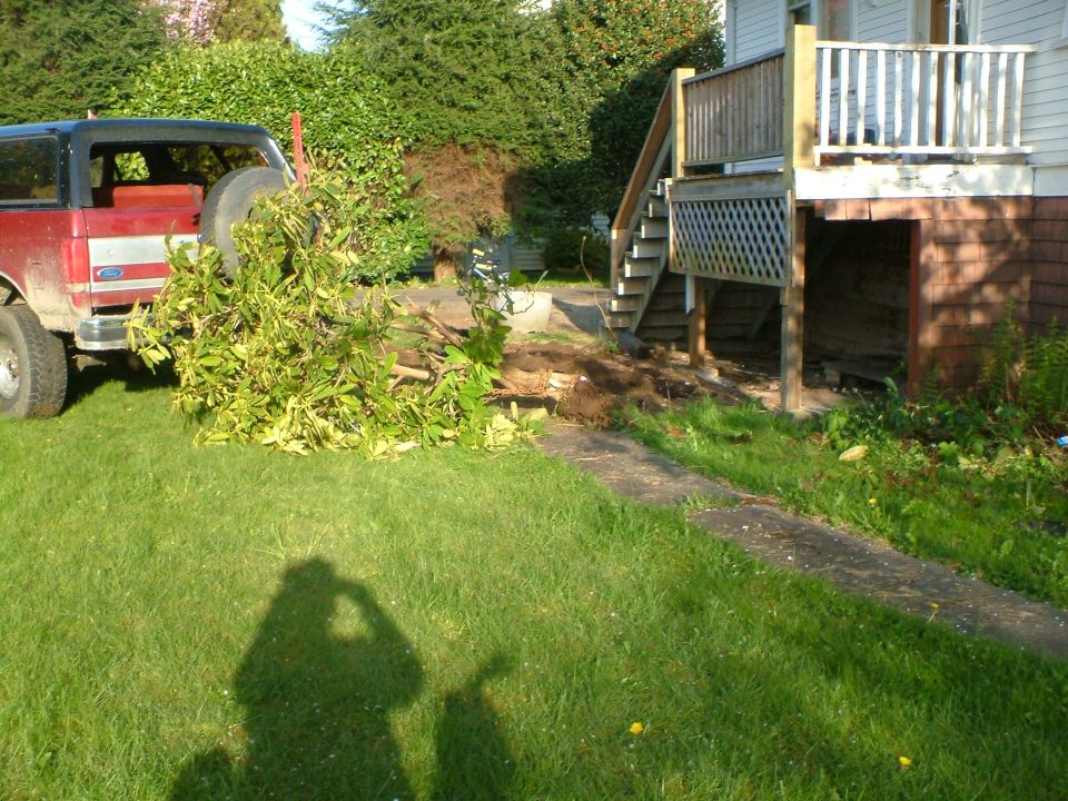 Red Ford Bronco with a spare tire on the back, parked on a grassy lawn next to a wooden deck