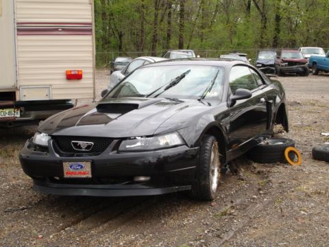 2001 Mercury Grand Marquis - Black Ford Mustang with missing front passenger wheel and a Ford Racing plate.