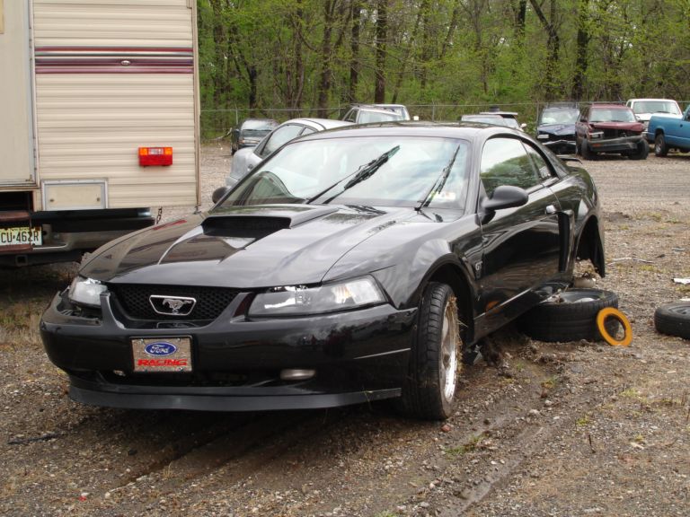 Black Ford Mustang with a scoop on the hood, missing front passenger wheel, and a Ford Racing plate on the grille