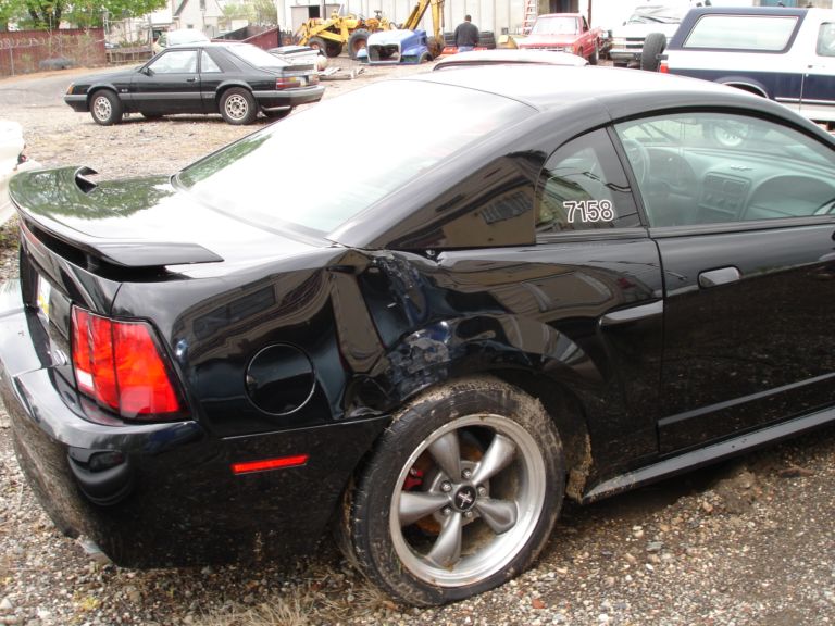 Black coupe with dented rear quarter panel and racing stripe