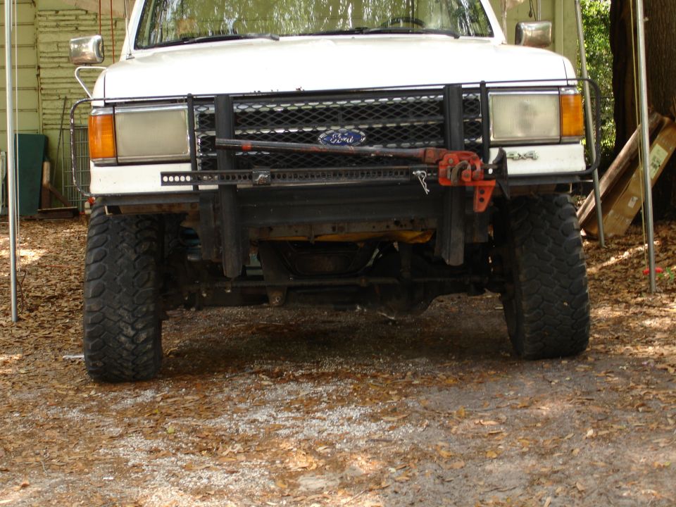 Front view of a white 1989 Ford Bronco with a bull bar and a Hi-Lift jack mounted on it