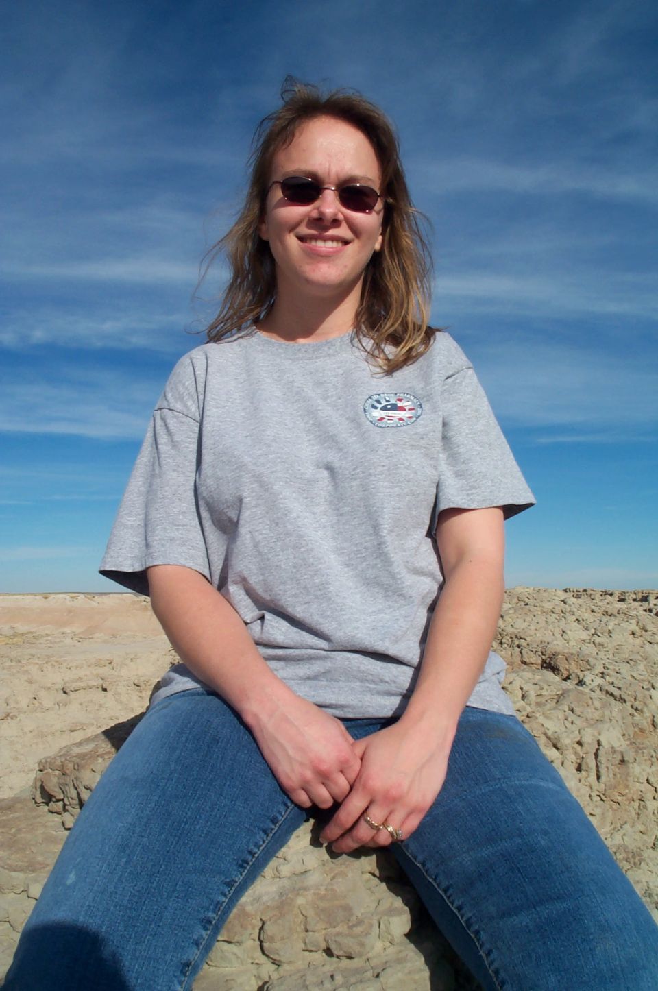 Woman in a grey t-shirt and blue jeans sitting on rocks outdoors