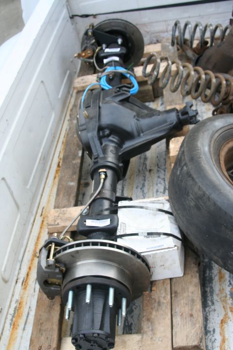 1992 Ford Bronco - Differential axle assembly with brake components and springs are visible in the back of a white pickup truck.