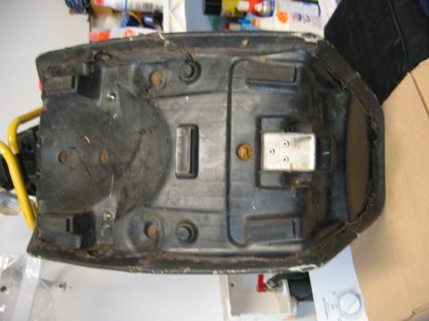 1985 Ford LTD Crown Victoria - The underside of a motorcycle seat base shows mounting points and some wear on the edges.