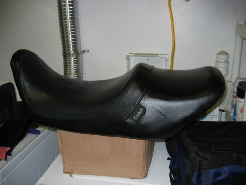1985 Ford LTD Crown Victoria - A black Corbin motorcycle seat rests on a cardboard box in front of a metallic pipe and a yellow cord.
