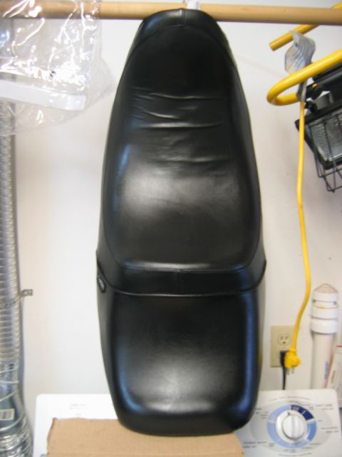 1985 Ford LTD Crown Victoria - Black motorcycle seat shown hanging indoors, with a washing machine and dryer visible.