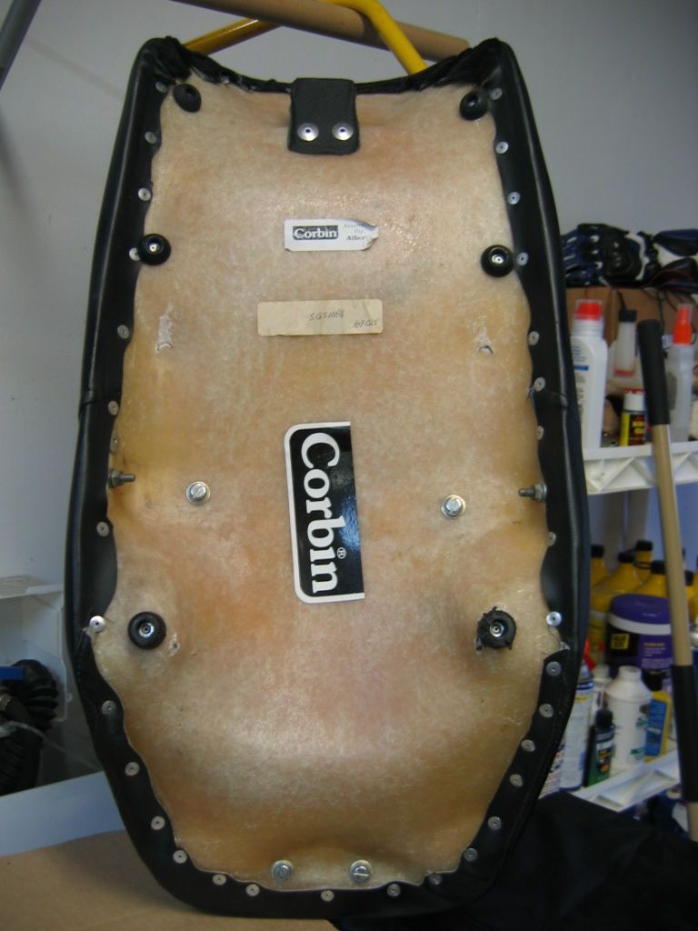 Underside of a Corbin motorcycle seat base with two stickers and visible hardware