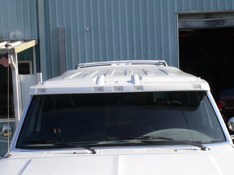 White truck roof with fiberglass sun visor, five cab lights and roof rack outside metal shop