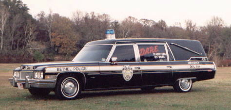 1998 Ford Crown Victoria - This police hearse, marked with 'Bethel Police' and 'DARE', sits on a grassy field with trees in the background.