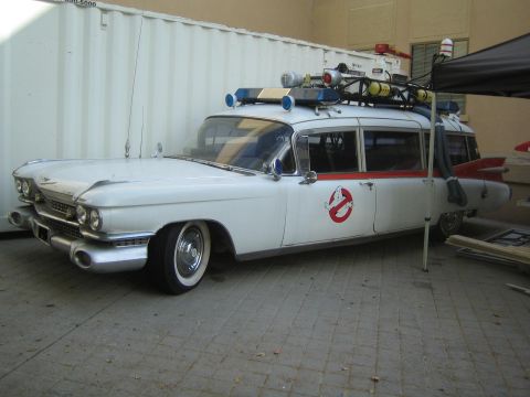 1990 Ford Bronco - Front three-quarter view of a white Cadillac with chrome grille, roof-mounted equipment, and a Ghostbusters logo, parked by a shipping cont…