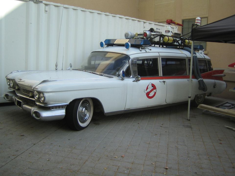 Front view of a white Cadillac Ecto-1 style car with roof gear by a container