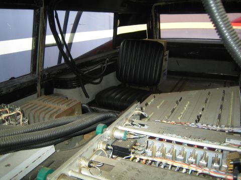 1990 Ford Bronco - Cluttered rear interior of a vehicle filled with bundled wiring, hoses, a heat sink, and a black vinyl seat resembling prop equipment.
