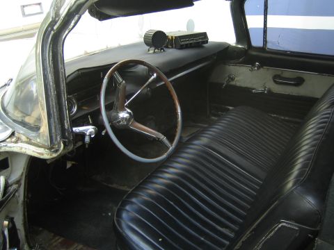 1990 Ford Bronco - Worn interior of an older car with a thin two-spoke steering wheel, dark dashboard, and a black vinyl bench seat.