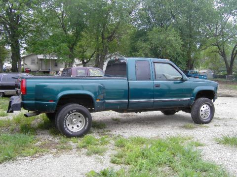 1995 GMC C/K Pickup - A teal green four-door pickup truck with dual rear wheels is parked on a gravel lot.