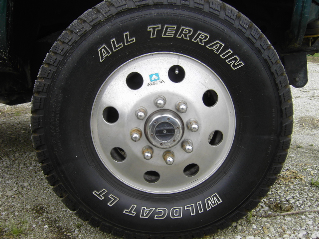 Truck wheel with 'ALL TERRAIN' and 'WILDCAT LT' tires. Silver hub with 8 lug nuts