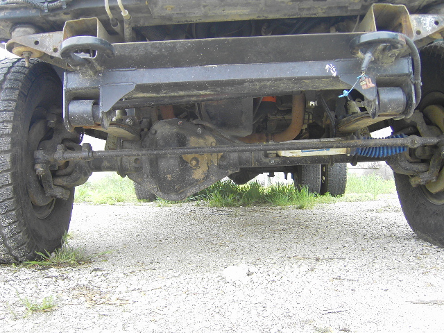 Undercarriage view of a truck showing the front differential, steering components, and exhaust pipe