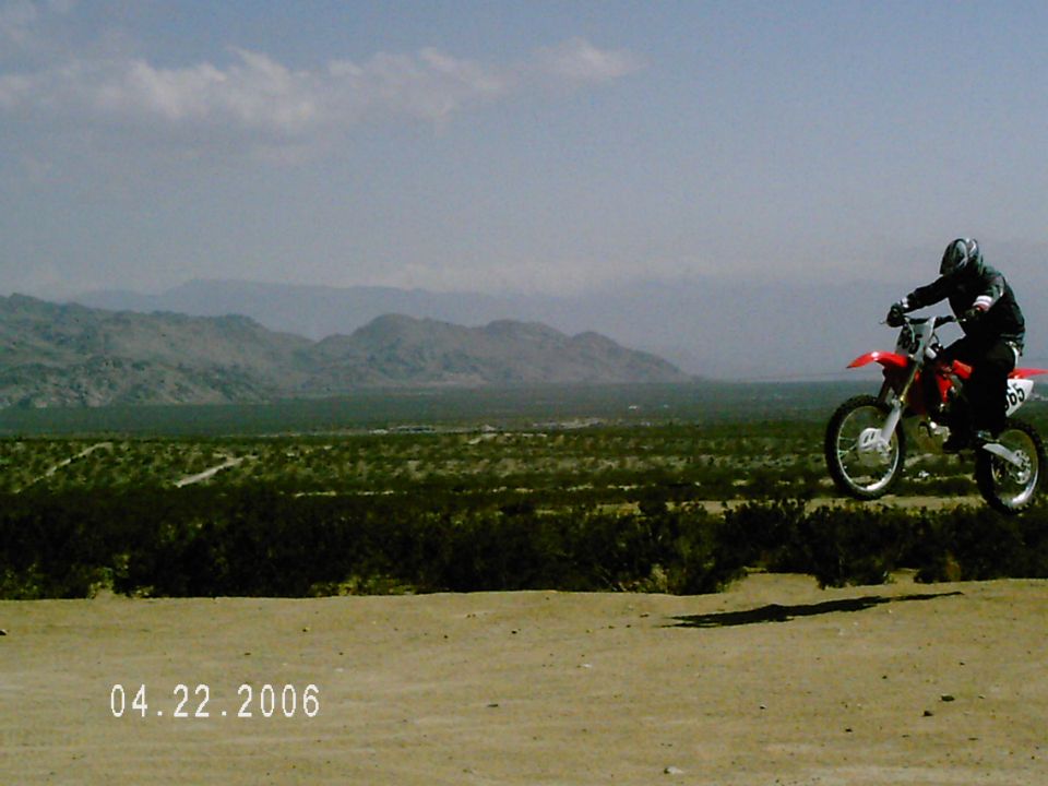 Rider jumping a red and white dirt bike over a desert rise