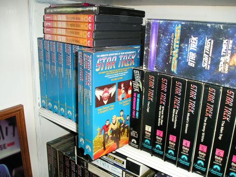 1984 Pontiac Fiero - A collection of Star Trek media, including VHS tapes and DVDs, is organized on shelves.
