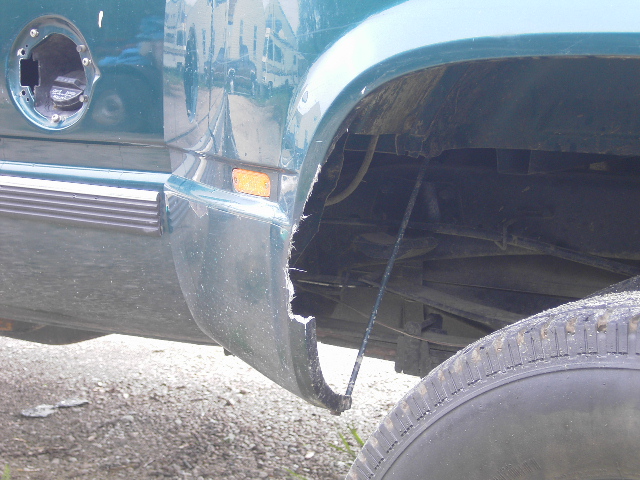 Green truck's rear fender is damaged, showing exposed undercarriage and tire