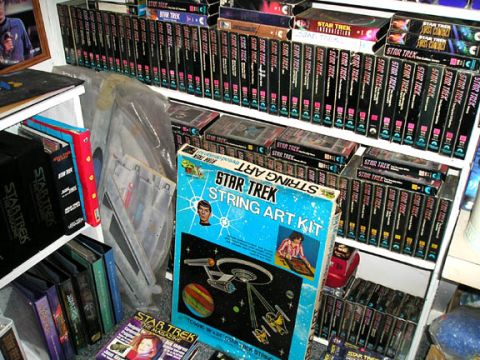 1984 Pontiac Fiero - A shelf filled with Star Trek memorabilia, including VHS tapes, books, and a string art kit, is displayed.