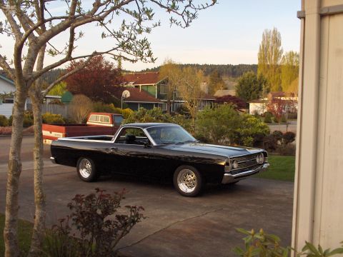 1968 Ford Ranchero - A black 1968 Ford Ranchero is parked in a driveway, with a red pickup truck visible behind it.