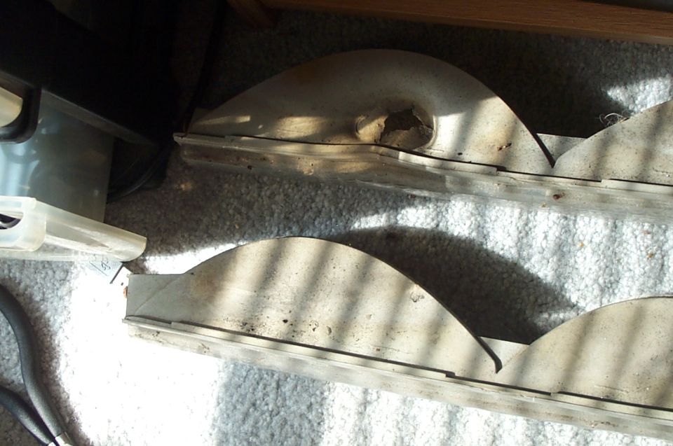 Two curved finned metal auto parts on gray carpet in sunlight