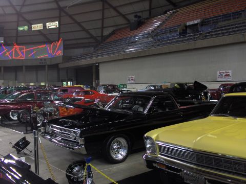 1968 Ford Ranchero - A black 1968 Ford Ranchero with flame decals is displayed at an indoor car show next to a yellow car.