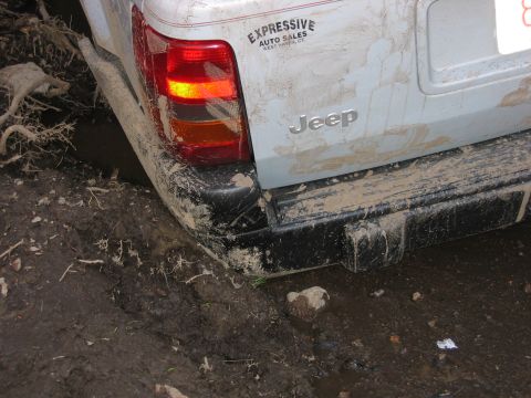 1995 Ford Bronco - A mud-splattered Jeep is stuck in a muddy ditch, with its rear bumper and taillight visible.